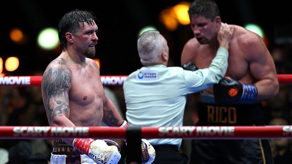 Referee Mark Lyson intervening to stop a boxing match, with Oleksandr Usyk walking away after a decisive moment.
