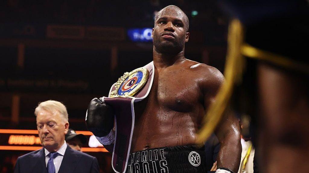 Daniel Dubois proudly displaying his WBO heavyweight title belt with promoter Frank Warren in the background.