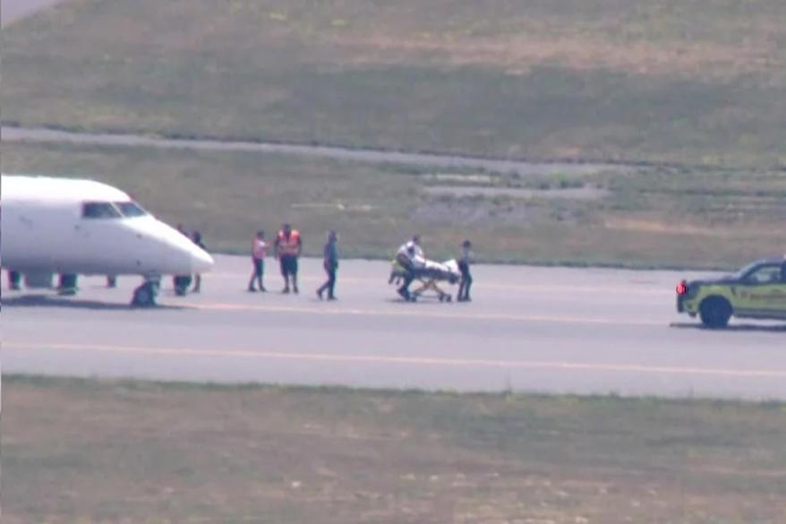 Emergency services personnel attending to the Air Canada flight on the runway at Boston Logan International Airport, with a stretcher visible near the cockpit.