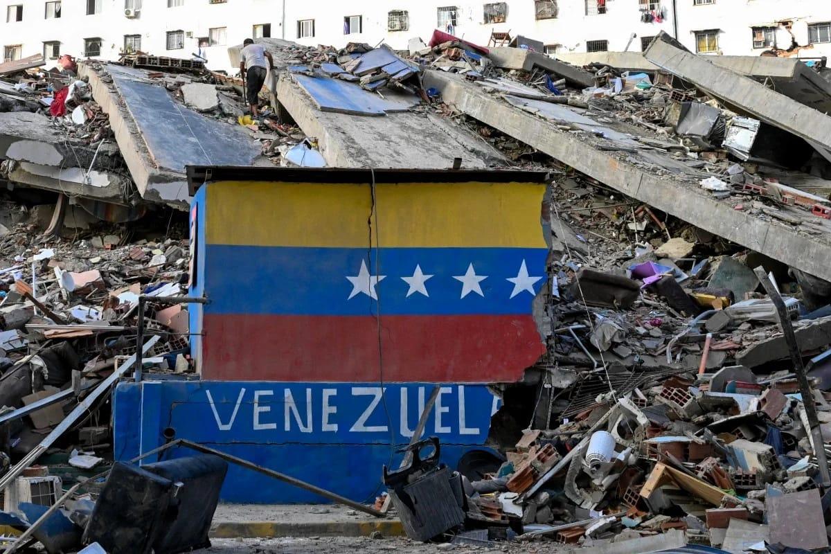 A close-up shot of a Venezuelan flag painted on a damaged wall, amidst the rubble of a collapsed building in Caraballeda, La Guaira state, following the June 26, 2026, earthquakes.