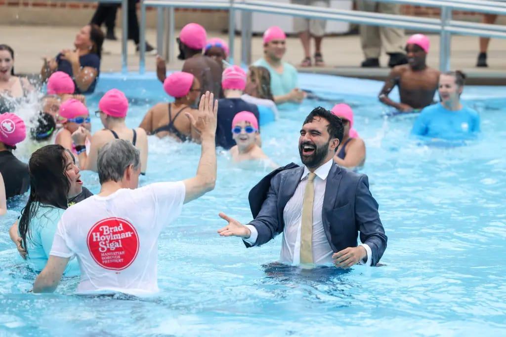 Mayor Zohran Mamdani engages with young swimmers after his fully clothed dive into a New York City public pool, defying city regulations on swimwear.