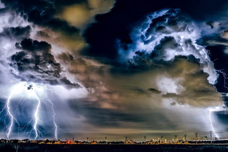 A powerful lightning bolt illuminates a dark, stormy sky, indicative of severe thunderstorms.