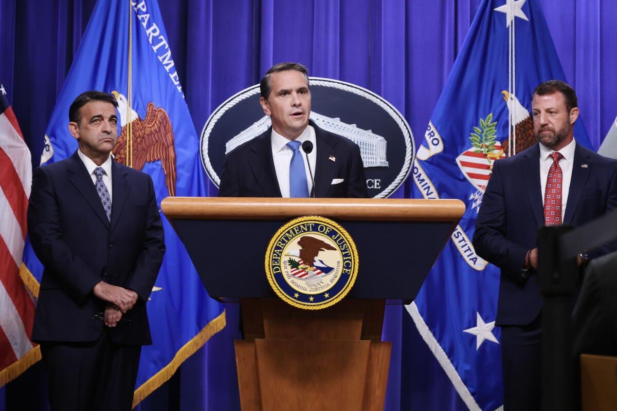 A man in a dark suit speaks at a podium, with a focused expression, suggesting a formal public address.