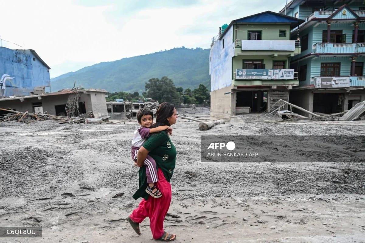 A woman carefully navigates a sludge-covered road with her child following flash floods in Devighat, Nepal, as rescue efforts continue.